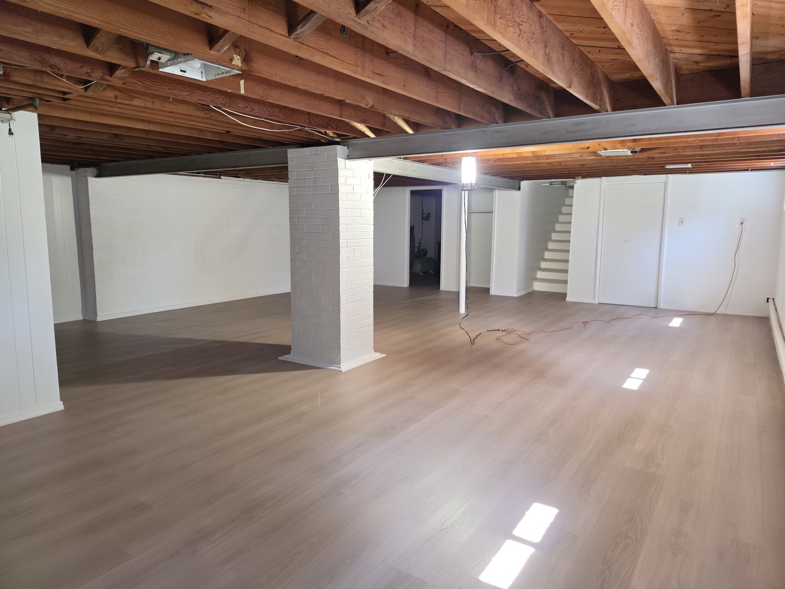 New LVP flooring in a basement with white masonry walls, columns and exposed ceiling joists