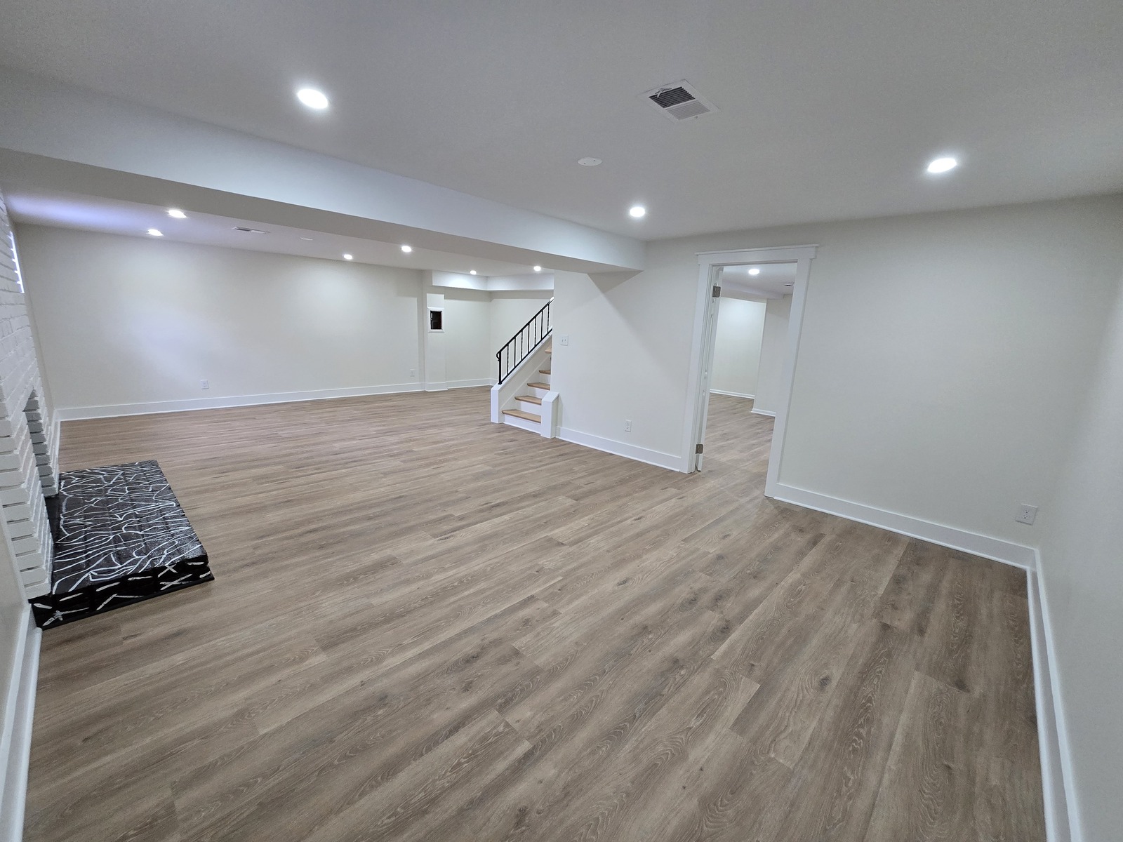 Bright basement with white walls, a light plank floor, stairs and recessed lights